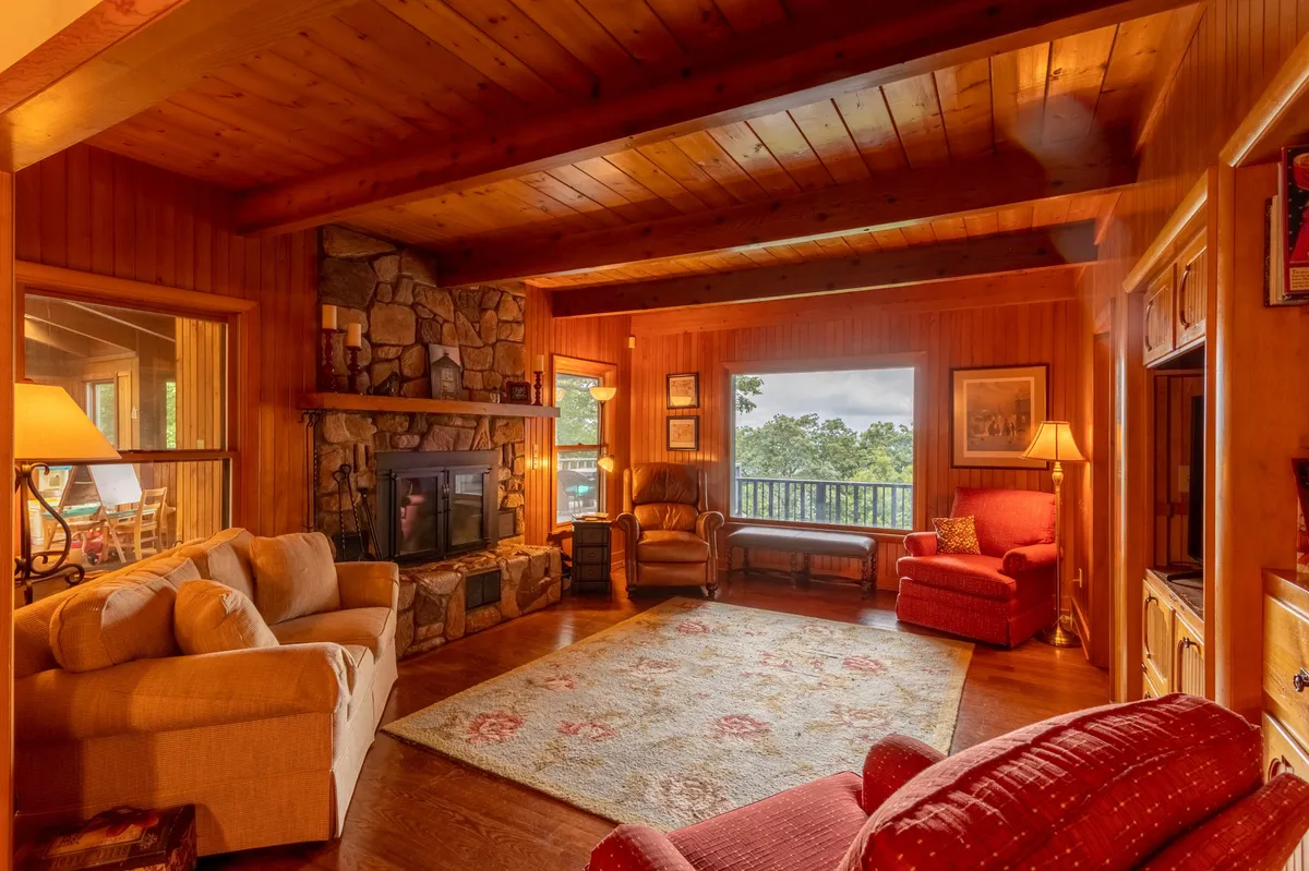 A welcoming living room with a prominent stone fireplace, large windows offering scenic views, and comfortable seating arranged for conversation or relaxation. The room's design invites gatherings around the fire or cozy evenings enjoying the surrounding landscape.