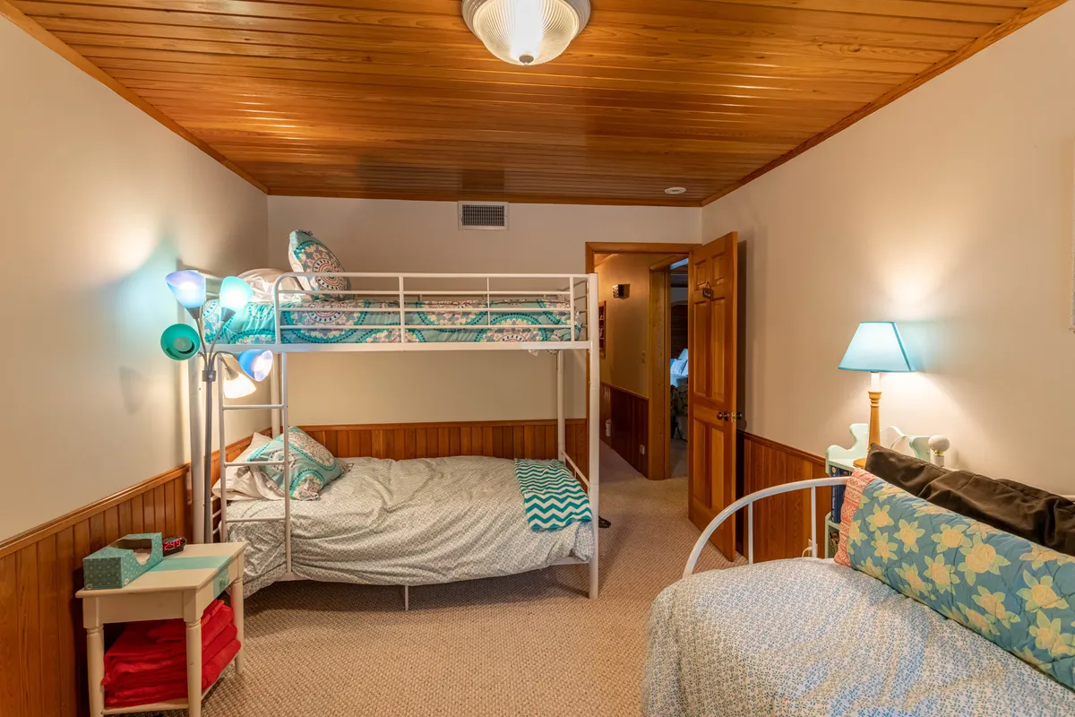 A welcoming family bedroom featuring a sturdy wooden bunk bed, a cozy sofa, a standing lamp, and playful wall decor. The space is bright and inviting, designed for comfort and adaptability—ideal for children or families sharing a room.