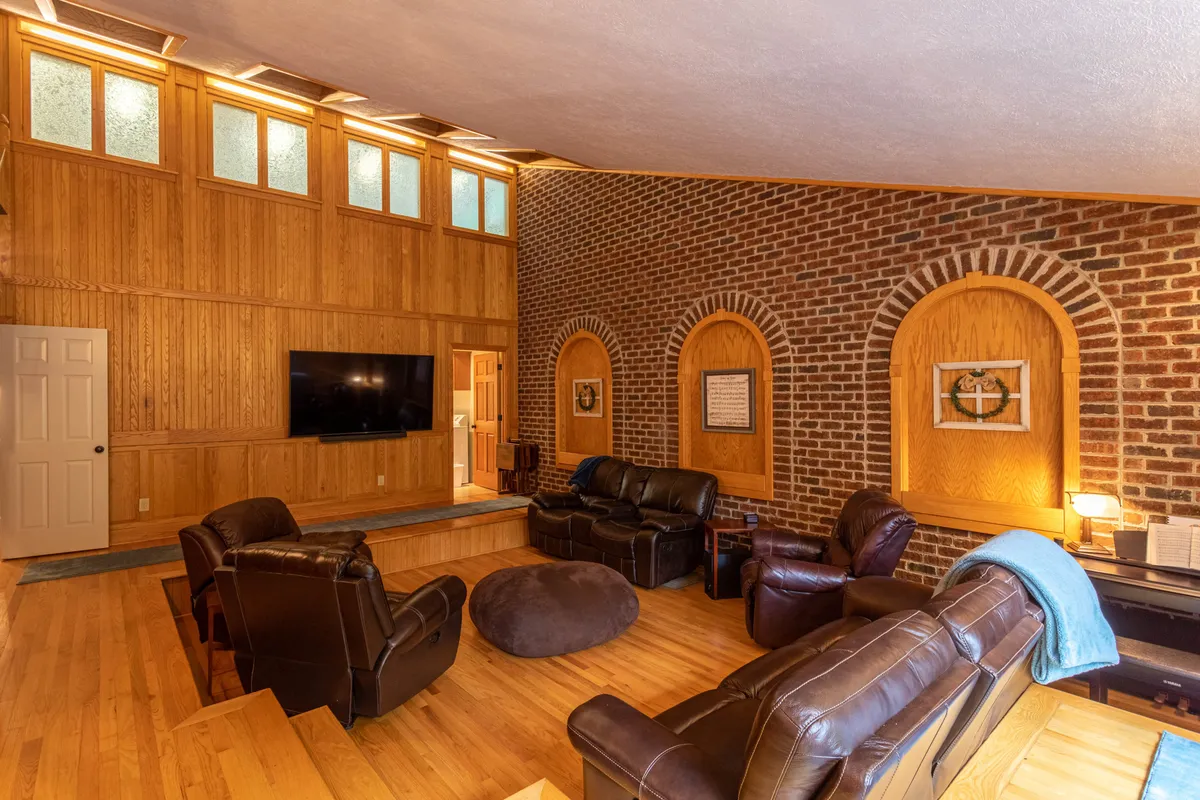 A plush, sunken theater room featuring tiered leather seating, a large television screen, and warm wood and brick accents. The layout is ideal for group movie nights or sporting events, creating a true cinematic experience in a home setting.