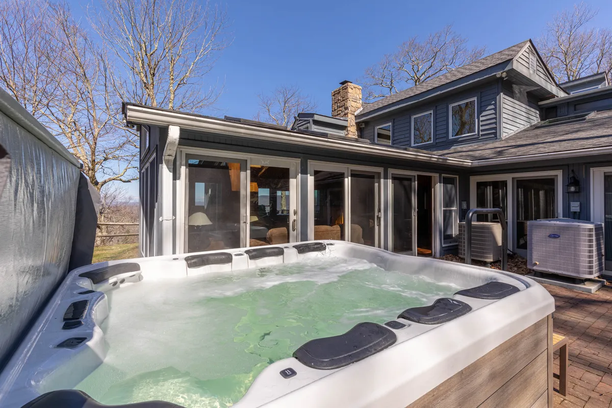 A modern hot tub is set on a stone patio beside the house, surrounded by lush landscaping and mountain views. The setting is tranquil and inviting, ideal for unwinding after a day of outdoor activities while soaking in the natural beauty.