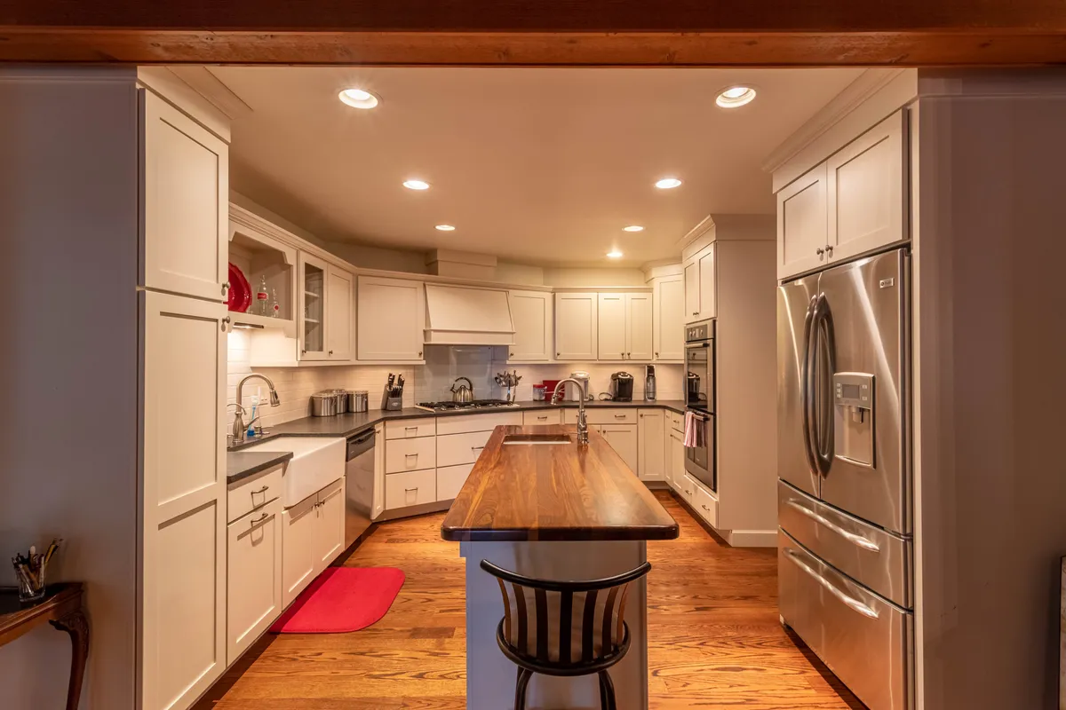 The image features a central kitchen island with a wooden countertop, gleaming stainless steel appliances, and an open-concept design that offers clear sightlines to the rest of the living area. The space is inviting and ready for entertaining, suggesting easy meal prep and group hospitality.
