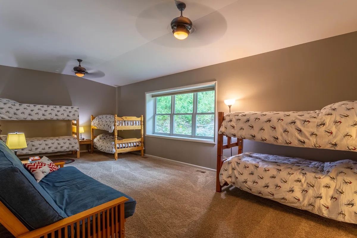 A cozy bunkroom with multiple bunk beds, a sofa, a large window, and a lamp. The design is inviting and practical, perfect for kids or teens to use as a hideout or for family sleepovers.