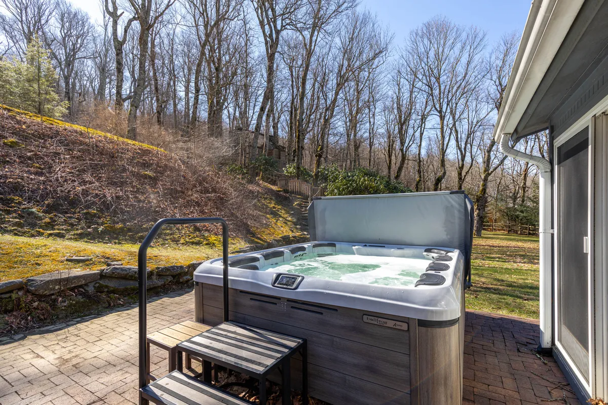 This exterior image showcases a bubbling hot tub nestled on a private patio, surrounded by lush trees. The tranquil setting emphasizes privacy and a direct connection to nature, inviting guests to relax and unwind outdoors.